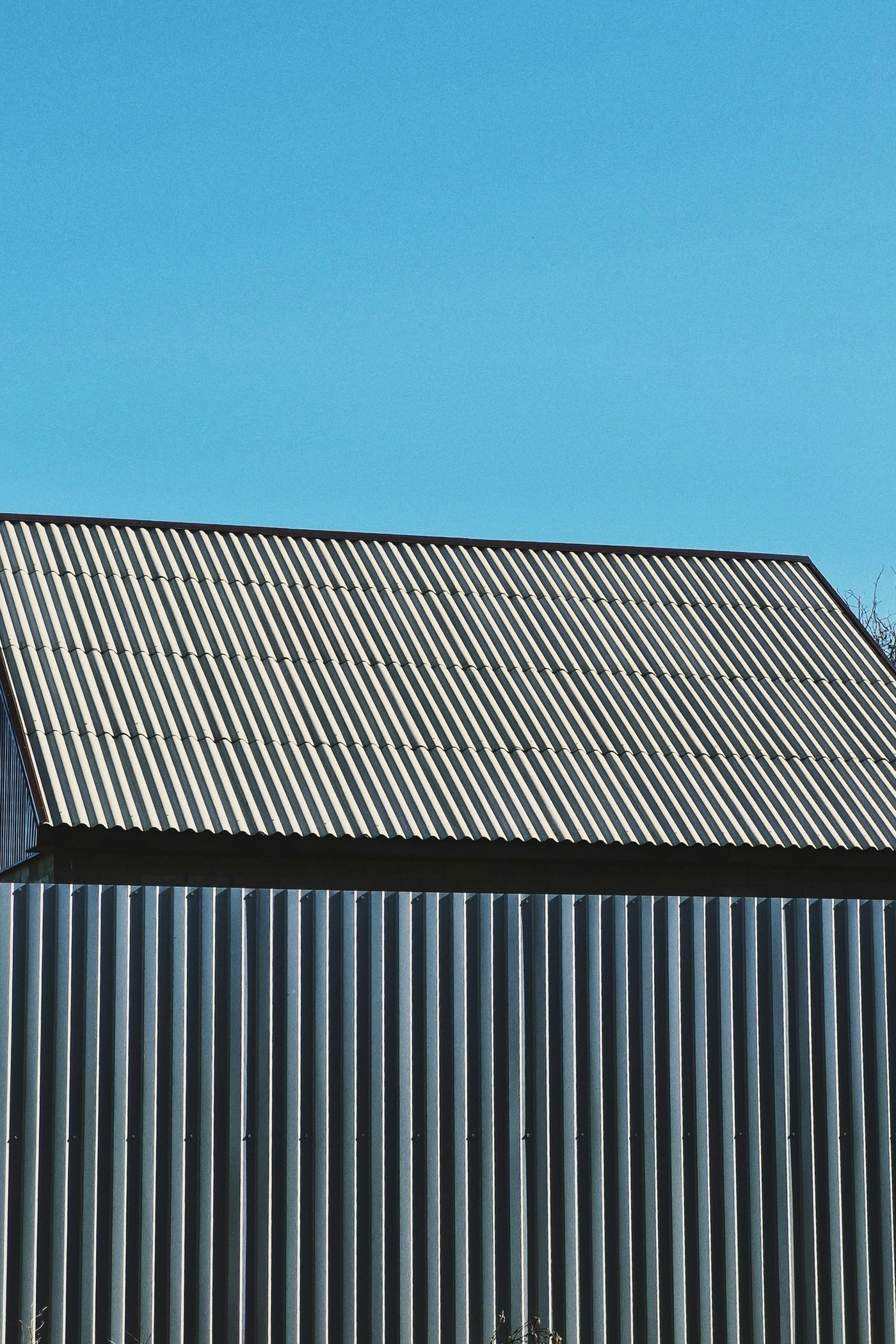 Corrugated metal roof and wall panels on a plain farm building under a clear sky.