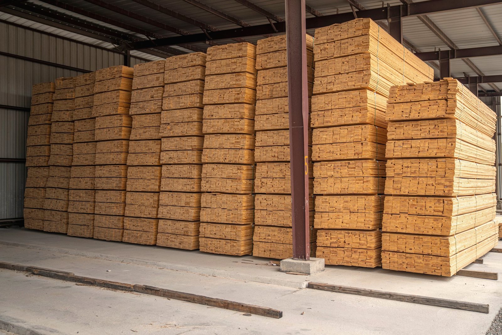 Inside a covered lumber shed, boards stacked from floor height up to the roof steel.