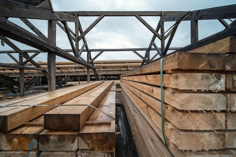 Heavy timbers stacked under an open shed truss.