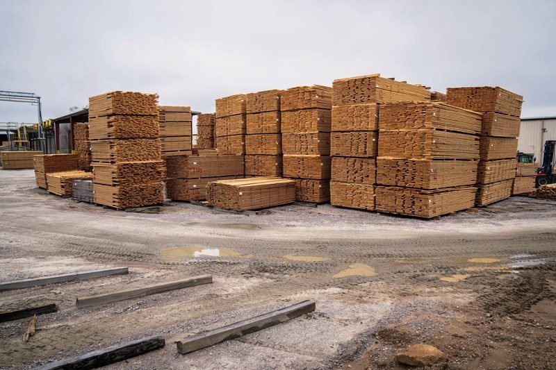 Banded units of dimensional lumber stacked across an open yard under a grey sky.